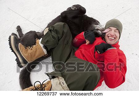 Stock Photo - Dog affectionately licking a man while lying on the snowcovered ground, Haines, Alaska. Fotosearch