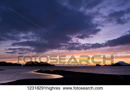 Stock Photograph - Dramatic sky at sunset over the ocean and silhouetted coastline; Sitka, Alaska, United States of America. Fotosearch