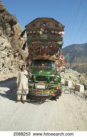 Stock Image - Driver Standing In Front Of His Painted And Decorated Pakistani Truck Near Dasu, North-West Frontier Province, Pakistan. Fotosearch