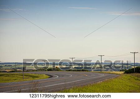 Stock Photograph - Electrical wires along a curving road with farmland in the distance; Saskatchewan, Canada. Fotosearch