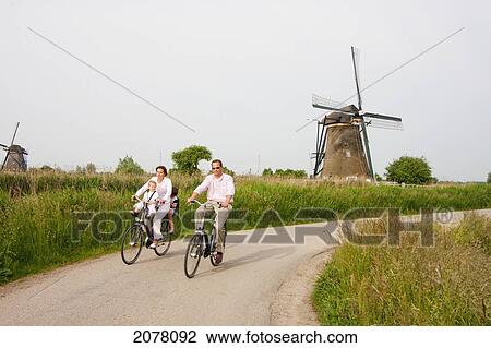 Stock Image - Family Cycling By Windmills, Built Around 1740 Along Nieuwe Waterschap To Drain The Excess Water From The Alblasserwaard Polders, Kinderdijk, Netherlands. Fotosearch