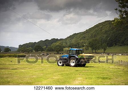 Stock Image - Farmer spreading fertilizer on meadow after taking crop of silage; Lancashire, England. Fotosearch