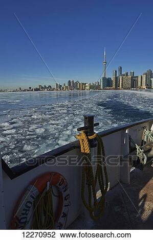 Stock Image - Ferry moving threw breaking ice in harbor waterfront; Toronto, Ontario, Canada. Fotosearch