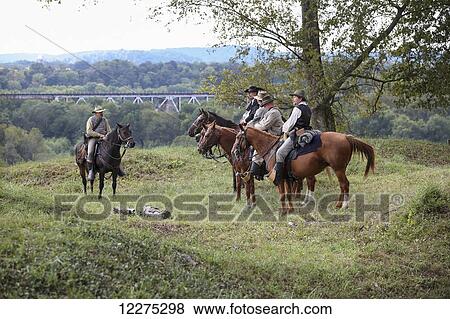 Stock Photo - Five American Civil War confederate re-enactors sitting on horses and discussing the battle with a railroad bridge in the background; United States of America. Fotosearch