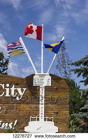 Stock Photo - Flags on the Mile Zero City Sign, the Start of Alaska Highway, Dawson Creek, British Columbia, Canada, Summer. Fotosearch