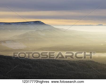 Stock Photograph - Fog settled over the snow covered landscape of the rugged Canadian Rockies and a forest in winter; British Columbia, Canada. Fotosearch