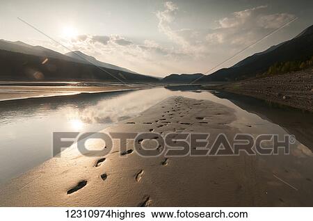 Stock Photograph - Footprints in the wet sand along a shore at sunset, Medicine Lake, Jasper National Park; Alberta, Canada. Fotosearch