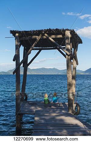 Girl and a boy sitting on the end of a jetty on Mumbo Island, Lake Malawi; Malawi View Large Photo Image Stock Photo - Girl and a boy sitting on the end of a jetty on Mumbo Island, Lake Malawi; Malawi. Fotosearch