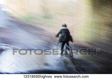 Stock Photograph - Girl rides her bike through high water in flood conditions. Fotosearch