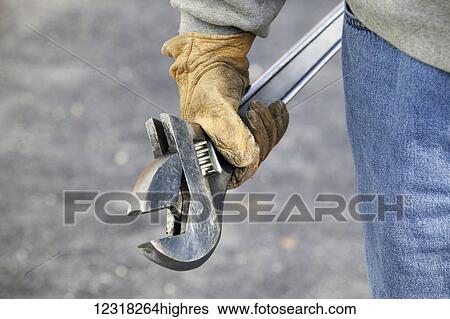 Stock Photograph - Gloved worker's hand with an adjustable wrench; New Holland, Pennsylvania, United States of America. Fotosearch