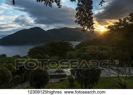 Stock Photograph - Golden sunlight glowing at sunset with a view of the coastline and lush foliage; Jalisco, Mexico. Fotosearch