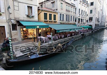 Stock Image - Gondola In A Canal By A Restaurant, Venice, Italy. Fotosearch