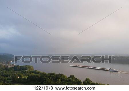 Stock Photo - Grain barge navigating the Mississippi River early on an overcast morning, near Hannibal; Missouri, United States of America. Fotosearch
