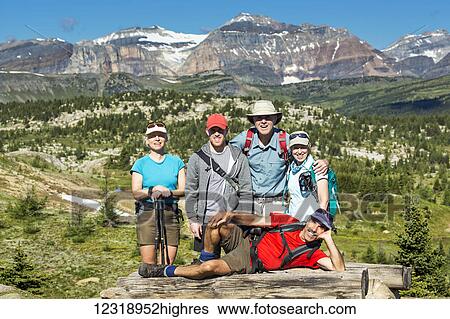 Stock Photograph - Group of hikers posing on a log bench with valley below and mountains and blue sky in the distance; Banff, Alberta, Canada. Fotosearch