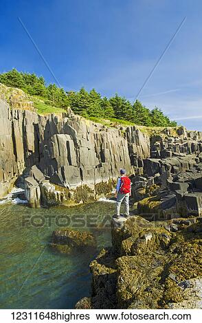 Stock Photograph - Hiker along basalt rock cliffs, Brier Island, Bay of Fundy; Nova Scotia, Canada. Fotosearch