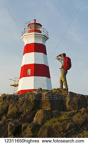 Stock Photograph - Hiker looking out over Brier Island Lighthouse, Bay of Fundy; Brier Island, Nova Scotia, Canada. Fotosearch