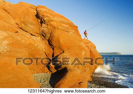 Stock Photograph - Hiker on the Red Rocks, Cape Chignecto Provincial Park, near Adocate in the Minas Basin, Bay of Fundy; Nova Scotia, Canada. Fotosearch