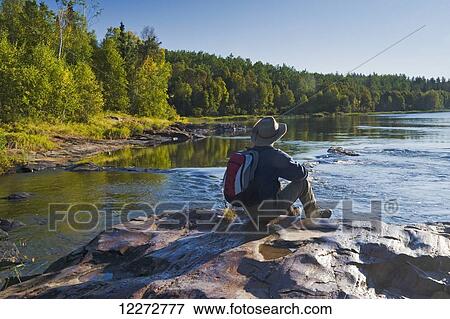 Stock Photo - Hiker resting along the Clearwater River in Clearwater River Provincial Park; Saskatchewan, Canada. Fotosearch