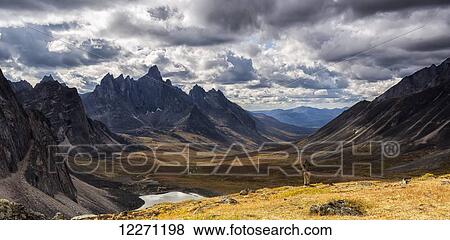 Stock Photo - Hiker standing on an overlook taking photos of the colourful valleys in Tombstone Territorial Park in autumn; Yukon, Canada. Fotosearch