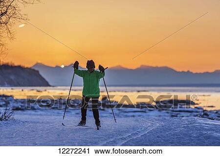 Stock Image - Hispanic woman back lit while cross country skiing on the Tony Knowles Coastal Trail at sunset, Southcentral Alaska. Fotosearch
