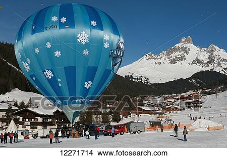 Picture - Hot air balloons floating high above snowy Bishop's Hat mountain peaks during the ski resort's annual hot air balloon festival; Filzmoos, Austria. Fotosearch