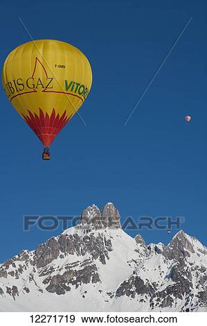 Stock Photo - Hot air balloons floating high above snowy Bishop's Hat mountain peaks during the ski resort's annual hot air balloon festival; Filzmoos, Austria. Fotosearch