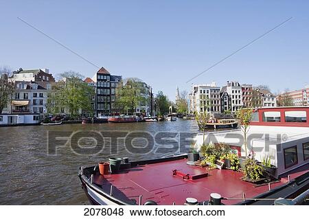 Stock Photo - Houseboat And Canal Houses By The Amstel River, Amsterdam, Netherlands. Fotosearch