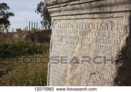 Stock Image - Inscribed Roman column with the Capitoline Temple in distance; Thuburbo Majus, Tunisia. Fotosearch
