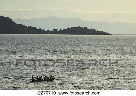 Stock Image - Large dugout canoe leaving Cape Maclear in the evening, Lake Malawi; Malawi. Fotosearch