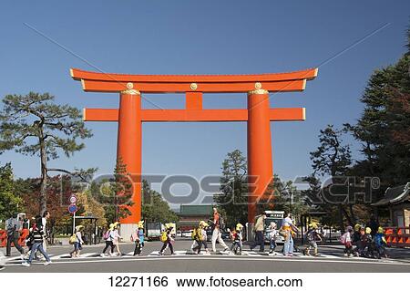 Stock Photograph - Large tori gate and pedestrians walking across the street; Kyoto, Japan. Fotosearch