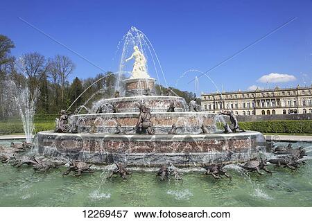 Stock Photo - Large water fountain with white statue on top and sculptures around it and a building in the background; Die Herreninsel im Chiemsee, Bayern, Germany. Fotosearch
