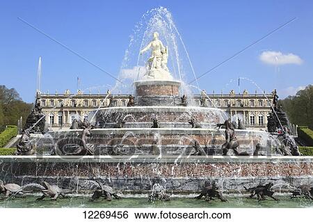 Stock Photograph - Large water fountain with white statue on top and sculptures around it and a building in the background; Die Herreninsel im Chiemsee, Bayern, Germany. Fotosearch
