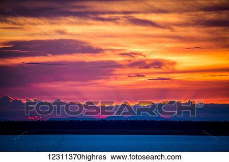 Stock Photograph - Light shines from behind clouds and mountains at sunset; Anchorage, Alaska, United States of America. Fotosearch