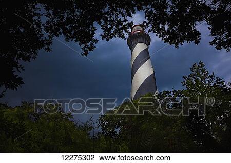Stock Image - Lighthouse viewed through the trees and vegetation with dark and moody clouds in the sky; St. Augustine, Florida, United States of America. Fotosearch