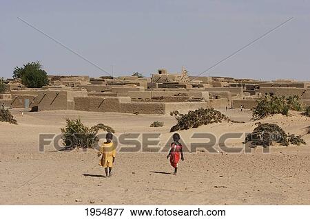 Stock Photo - Little girls walking with built structures in the bachground at Sebi, Mali. Fotosearch