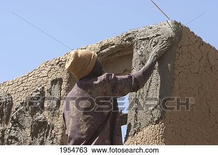 Stock Image - Man applying mud to a house, Djenne, Mali. Fotosearch