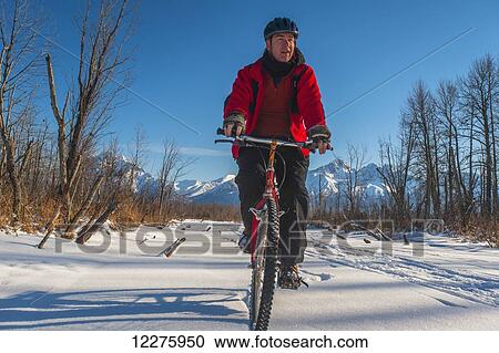 Stock Image - Man bicycling on frozen Rabbit Creek in the Palmer Haystack Game Refuge with Chugach Mountains in the background, Southcentral Alaska, winter. Fotosearch