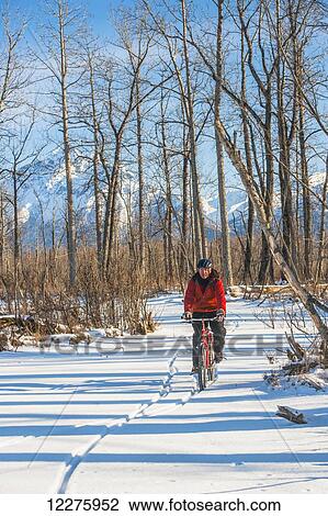 Stock Image - Man bicycling on frozen Rabbit Creek in the Palmer Haystack Game Refuge with Chugach Mountains in the background, Southcentral Alaska, winter. Fotosearch