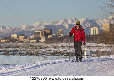 Stock Photography - Man cross country skiing on the Tony Knowles Coastal Trail near Earthquake Park with Anchorage skyline in the background, Cook Inlet, Southcentral Alaska. Fotosearch