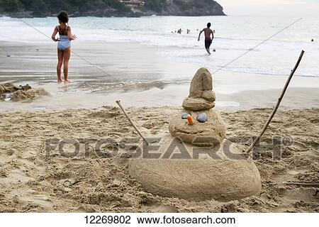 Stock Image - Man made of sand on the beach and people playing in the water; Guerrero, Mexico. Fotosearch