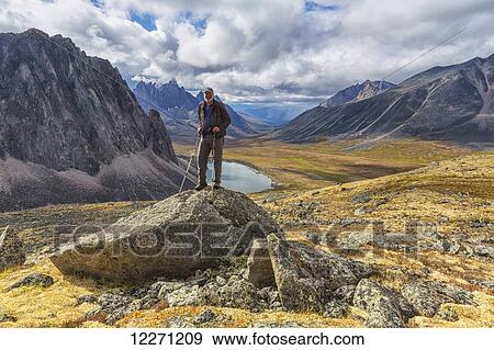 Stock Photo - Man standing on a rock overlooking the granite peaks of Tombstone Territorial Park in autumn; Yukon, Canada . Fotosearch