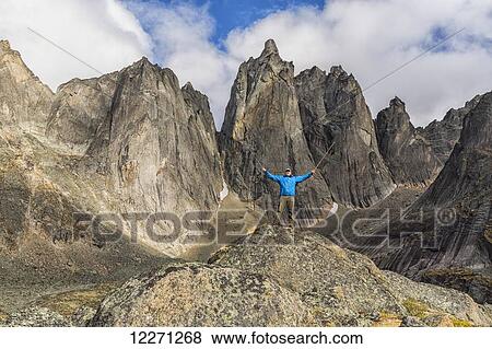 Stock Photo - Man standing on a rock overlooking the jagged granite peaks of Tombstone Territorial Park; Yukon, Canada . Fotosearch