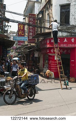 Picture - Man uses a ladder in a dangerous way close to the street wires, Xiamen local market; Xiamen, Fujian Province, China. Fotosearch