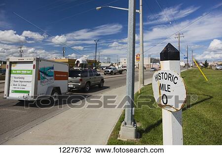 Stock Image - Mile Zero of the Alaska Highway, a car driving by in the background, Dawson Creek, British Columbia, Canada, Summer. Fotosearch