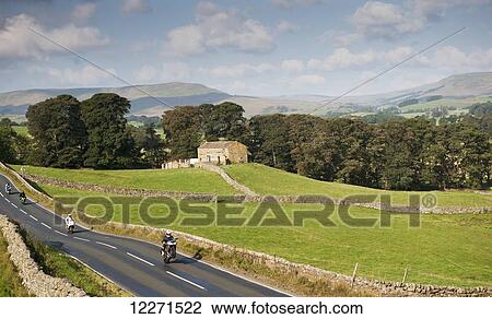 Stock Image - Motorcyclists on rural road speeding and doing a wheelie; Wenslydale, North Yorkshire, England. Fotosearch