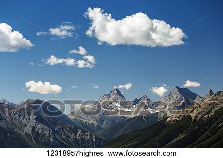 Stock Photograph - Mountain range with fluffy clouds and blue sky, Banff National Park; Banff, Alberta, Canada. Fotosearch