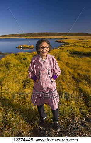 Stock Photography - Native Alaskan elder woman wearing an Atigik standing on the Tundra with a small lake in the background, Fall, Kotzbue, Arctic Alaska, USA.. Fotosearch