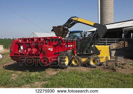 New Holland L180 skid steer loader loading manure into New Holland M2090 attached to T7060 tractor; New Holland, Pennsylvania, United States of America View Large Photo Image Stock Image - New Holland L180 skid steer loader loading manure into New Holland M2090 attached to T7060 tractor; New Holland, Pennsylvania, United States of America. Fotosearch