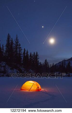 Picture - Nighttime view of a lit tent on a snow covered Trail Lake with the moon, stars, and planets overhead, Moose Pass, Kenai Peninsula, Southcentral Alaska. Fotosearch