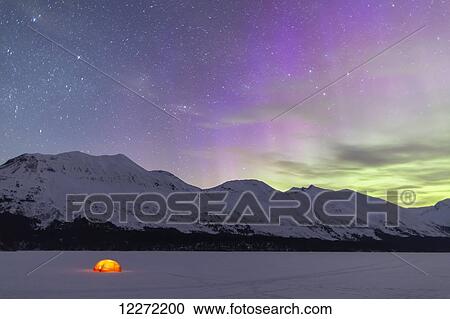Stock Image - Nighttime view of a lit tent on a snow covered Trail Lake with the moon, stars, and Northern Lights overhead, Moose Pass, Kenai Peninsula, Southcentral Alaska. Fotosearch